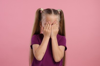 Resentful girl covering her face with hands on pink background