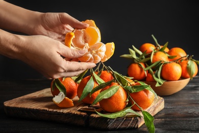Photo of Woman peeling ripe tangerine over table on dark background, closeup