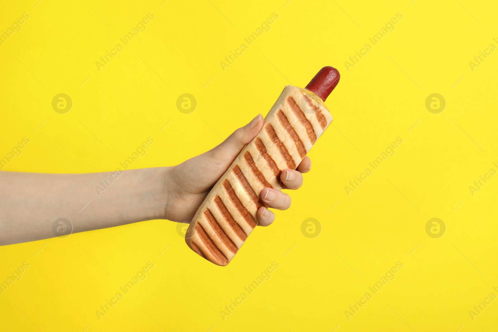 Photo of Woman holding delicious french hot dog on yellow background, closeup