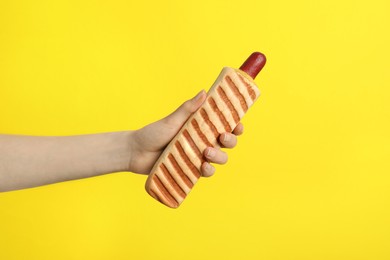 Photo of Woman holding delicious french hot dog on yellow background, closeup