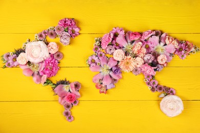 World map made of different beautiful flowers on yellow wooden table, flat lay