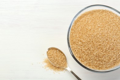 Photo of Brown sugar in bowl and spoon on white wooden table, flat lay. Space for text