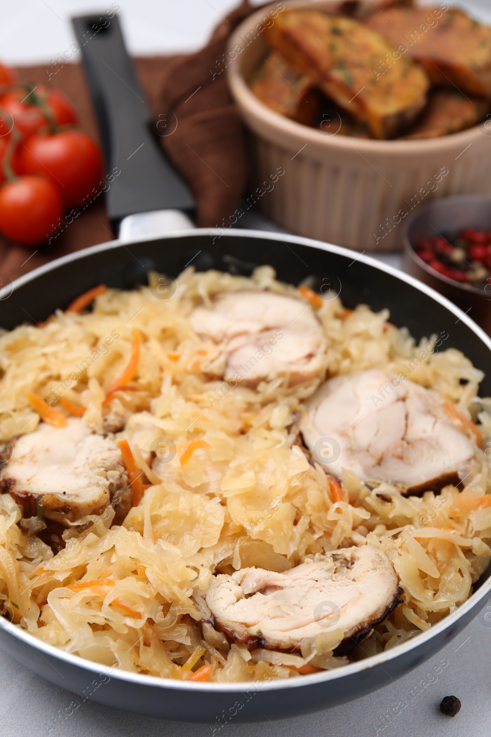 Photo of Frying pan with sauerkraut and chicken on white table, closeup