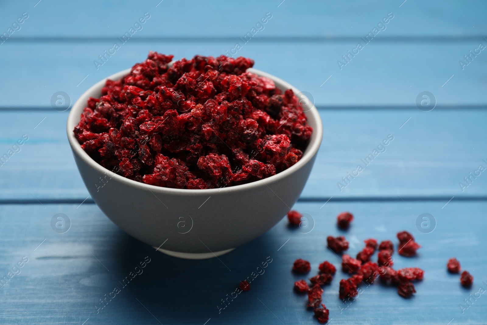 Photo of Bowl of dried red currant berries on blue wooden table