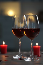 Glasses of red wine and burning candles on grey table against blurred lights, space for text. Romantic atmosphere