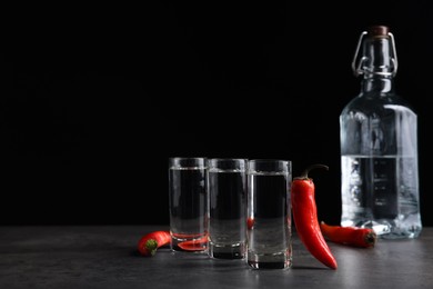 Photo of Red hot chili peppers and vodka on grey table against black background, space for text