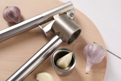 Photo of Metal press and garlic on white table, closeup