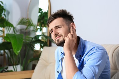 Photo of Young man suffering from ear pain at home. Space for text