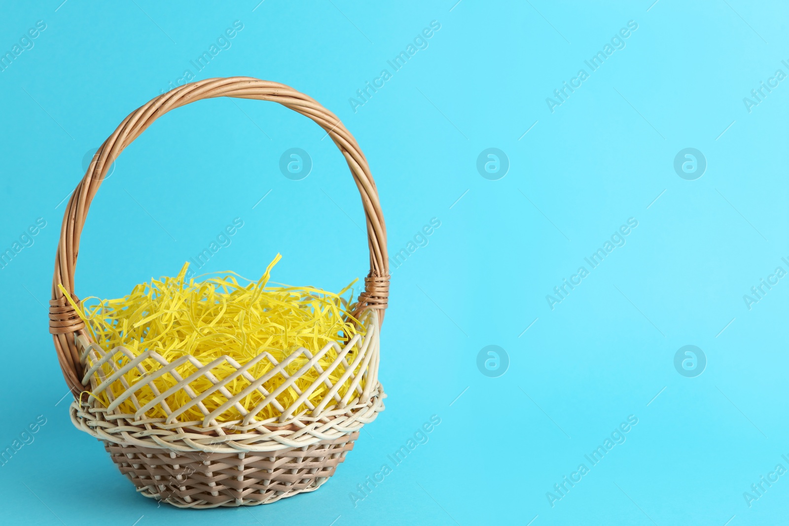 Photo of Easter basket with yellow paper filler on light blue background, space for text