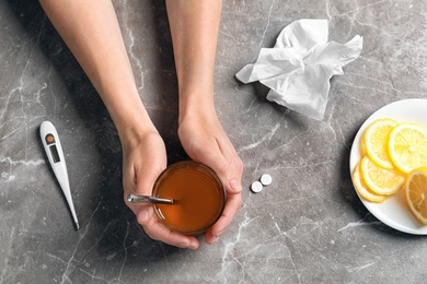 Photo of Woman holding glass with hot tea for cold on table, top view