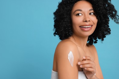 Photo of Young woman applying body cream onto shoulder on light blue background. Space for text