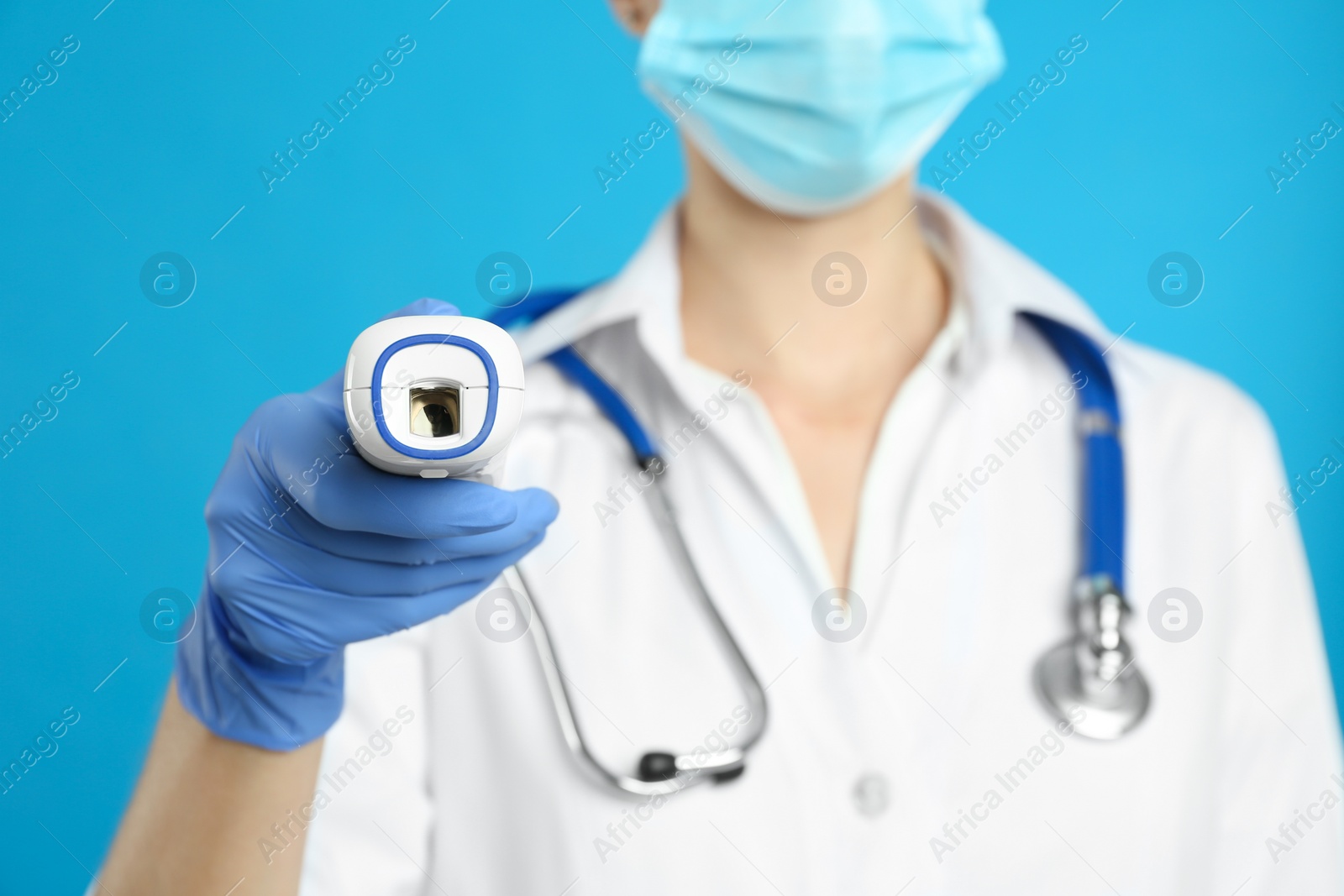 Photo of Doctor holding non contact infrared thermometer against light blue background, focus on hand. Measuring temperature
