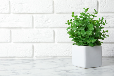 Photo of Beautiful artificial plant in flower pot on white marble table near brick wall. Space for text