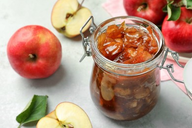 Photo of Tasty apple jam in glass jar and fresh fruits on light table