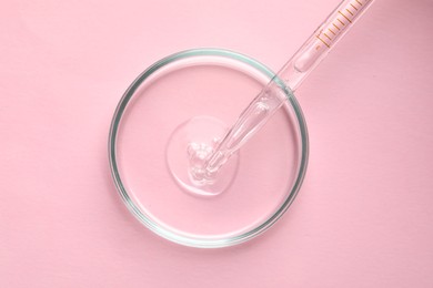 Glass pipette and petri dish with liquid on pink background, top view