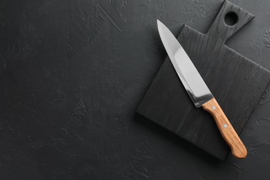 Photo of One sharp knife and board on dark textured table, top view. Space for text