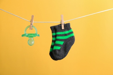 Small socks and pacifier hanging on washing line against color background. Baby accessories