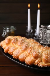 Photo of Homemade braided bread with sesame seeds, goblet and candles on wooden table, closeup. Traditional Shabbat challah