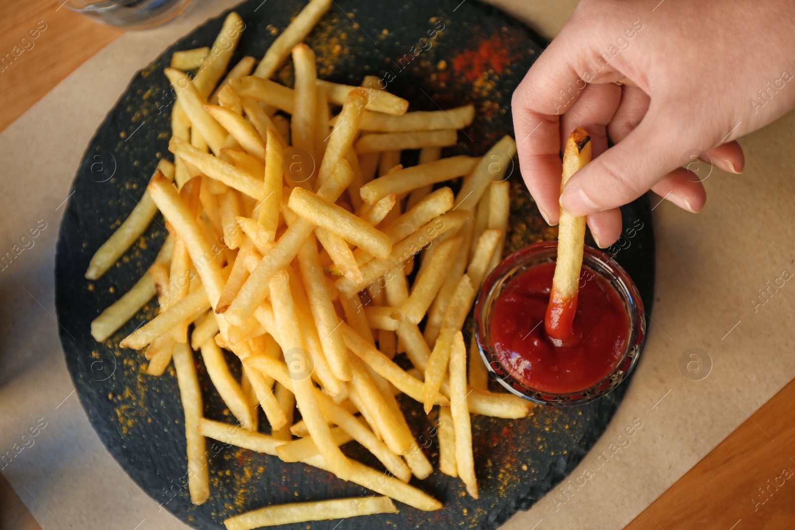 Photo of Woman dipping French fries into red sauce in cafe, closeup