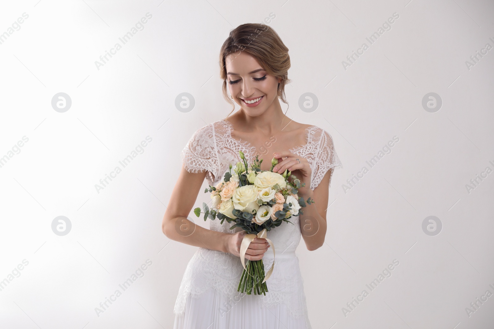 Photo of Young bride with elegant hairstyle holding wedding bouquet on white background