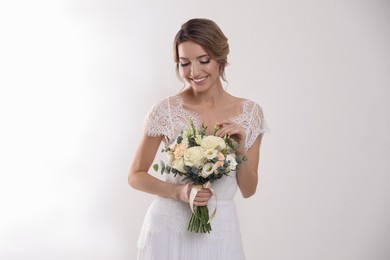 Photo of Young bride with elegant hairstyle holding wedding bouquet on white background