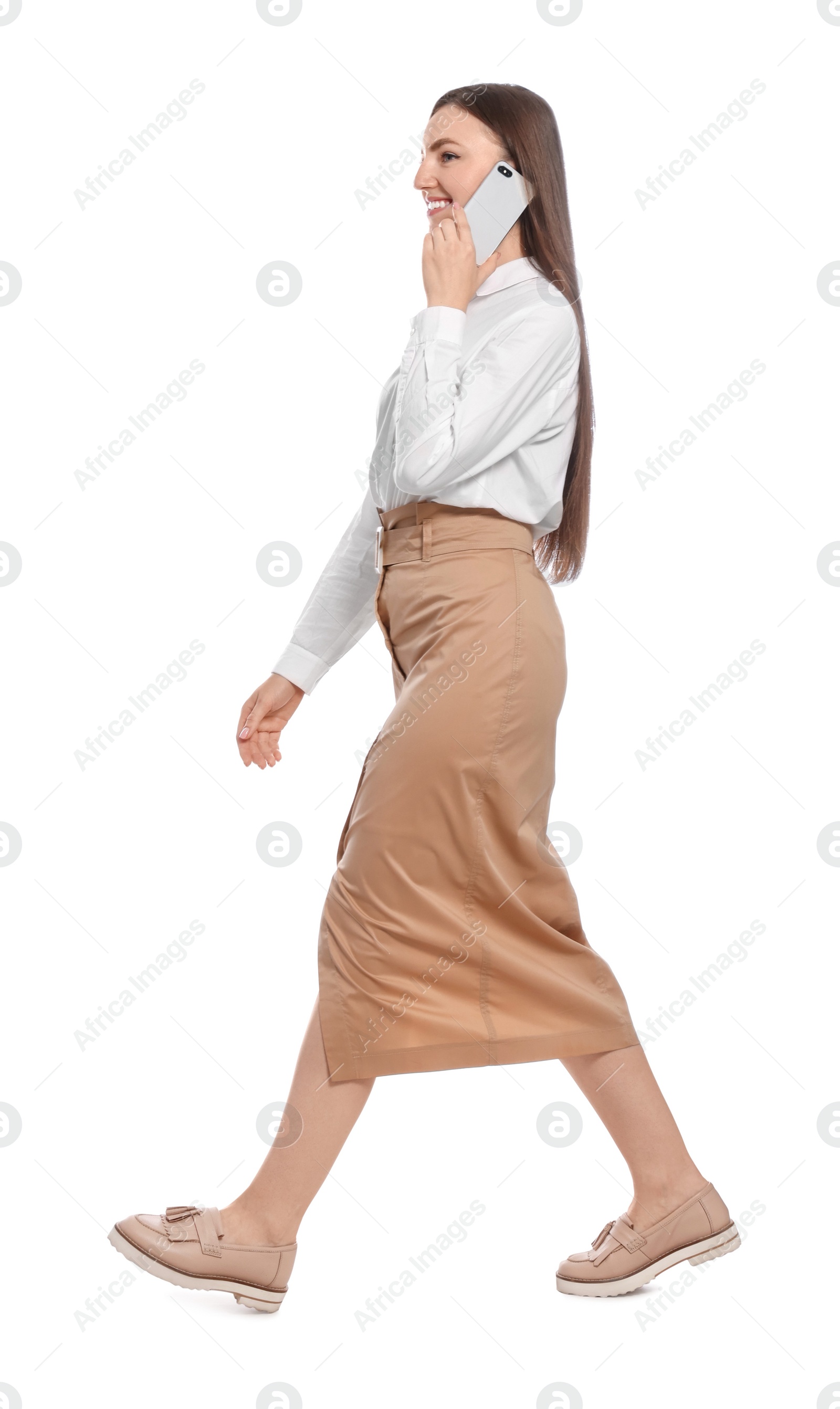 Photo of Young woman in casual outfit talking on smartphone while walking against white background