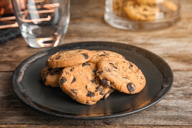 Photo of Plate with tasty chocolate chip cookies on wooden table