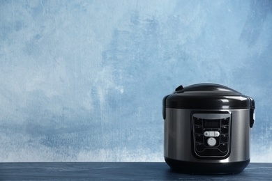 Photo of Modern powerful multi cooker on table against color background. Space for text