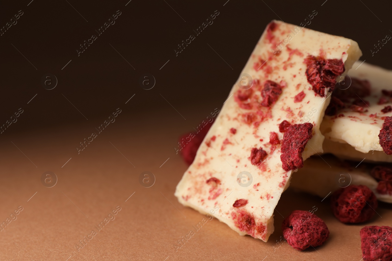 Photo of White chocolate with freeze dried raspberries on brown table, closeup. Space for text