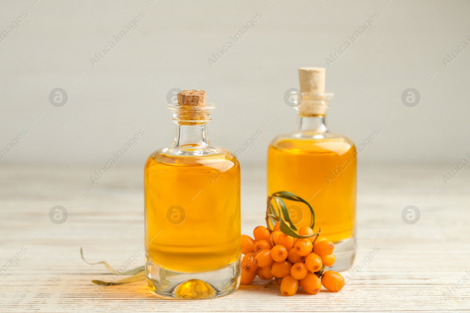 Photo of Natural sea buckthorn oil and fresh berries on white wooden table