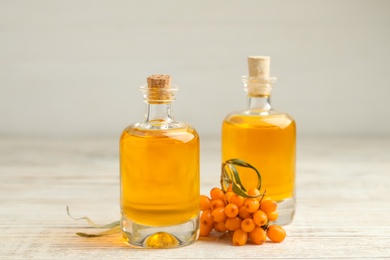 Photo of Natural sea buckthorn oil and fresh berries on white wooden table