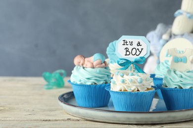 Photo of Beautifully decorated baby shower cupcakes for boy with cream on white wooden table. Space for text