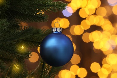 Photo of Beautiful blue bauble hanging on Christmas tree against blurred festive lights, closeup