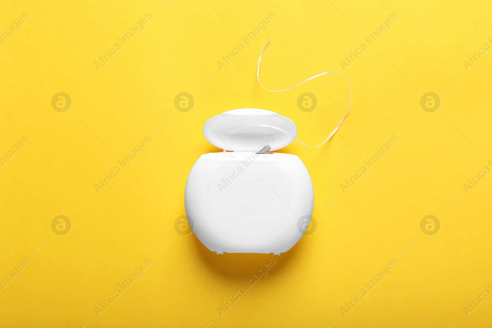 Photo of Container with dental floss on yellow background, top view