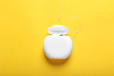 Photo of Container with dental floss on yellow background, top view