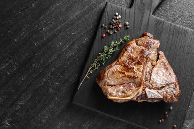 Photo of Delicious fried beef meat, thyme and peppercorns on black table, top view. Space for text