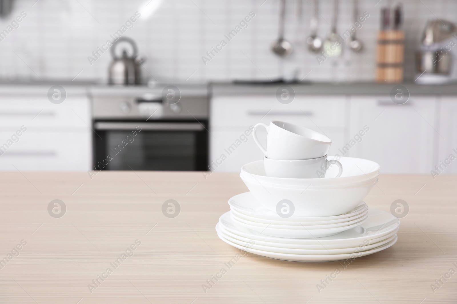 Photo of Stack of clean dishes and cups on table against blurred background. Space for text