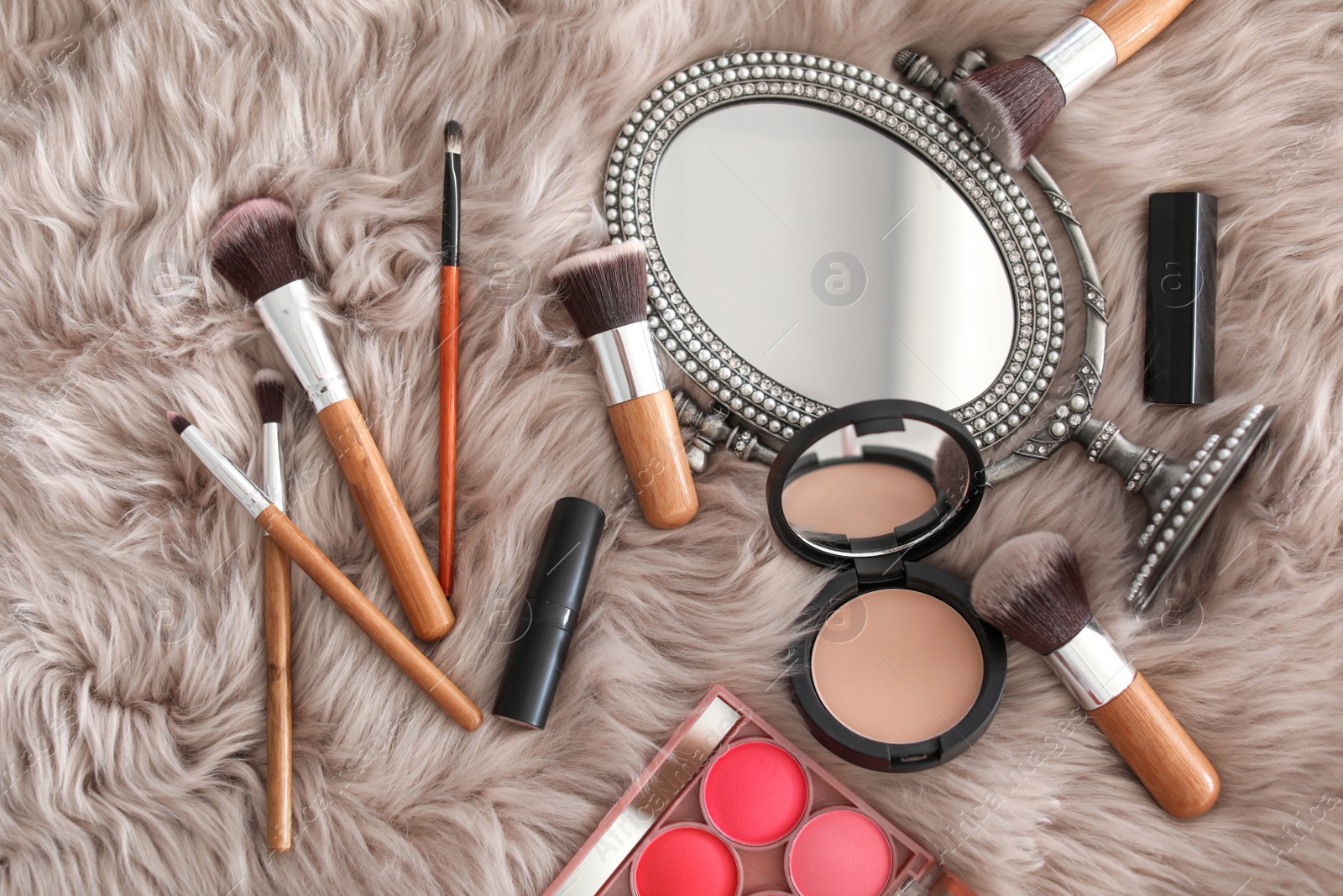 Photo of Flat lay composition with makeup brushes, cosmetic products and mirror on faux fur