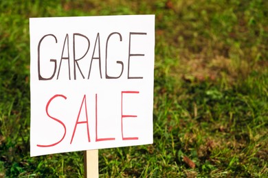 Photo of Sign Garage sale written on cardboard near grass, closeup. Space for text