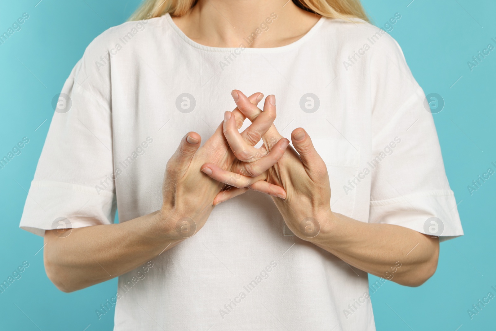 Photo of Woman cracking her knuckles on turquoise background, closeup. Bad habit