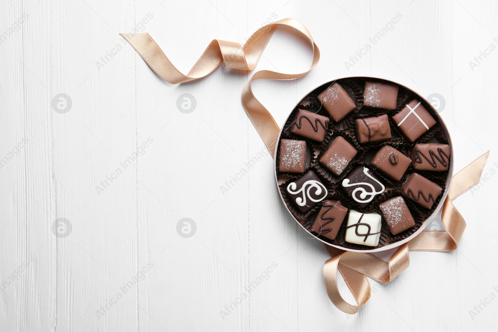 Photo of Delicious chocolate candies in box on white wooden table, flat lay. Space for text