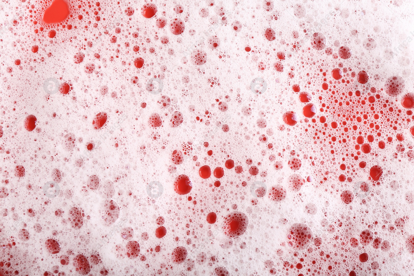 Photo of White foam with bubbles on red background, top view