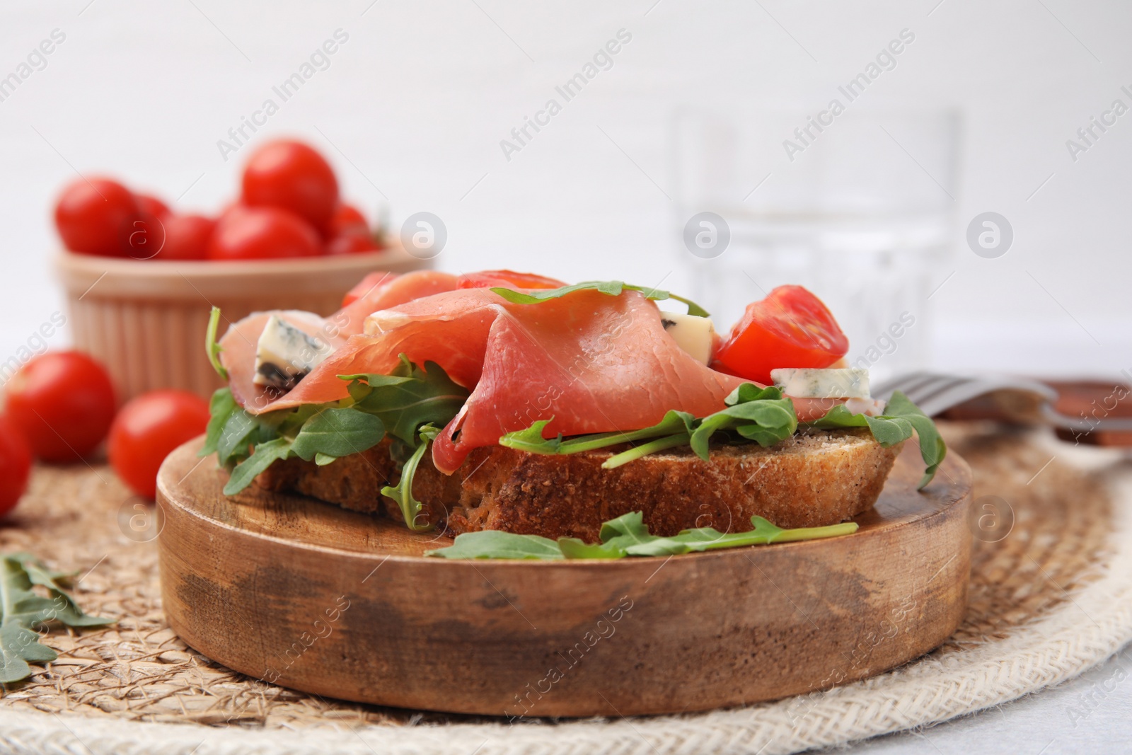 Photo of Tasty bruschetta with prosciutto, arugula, cheese and tomato on wooden board