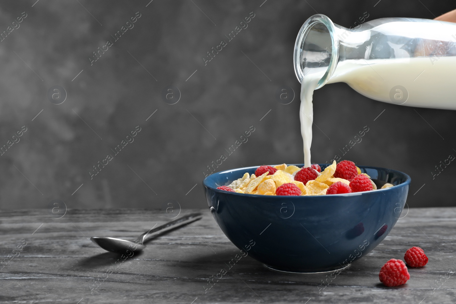 Photo of Pouring milk into bowl with cornflakes on dark table. Whole grain cereal for breakfast