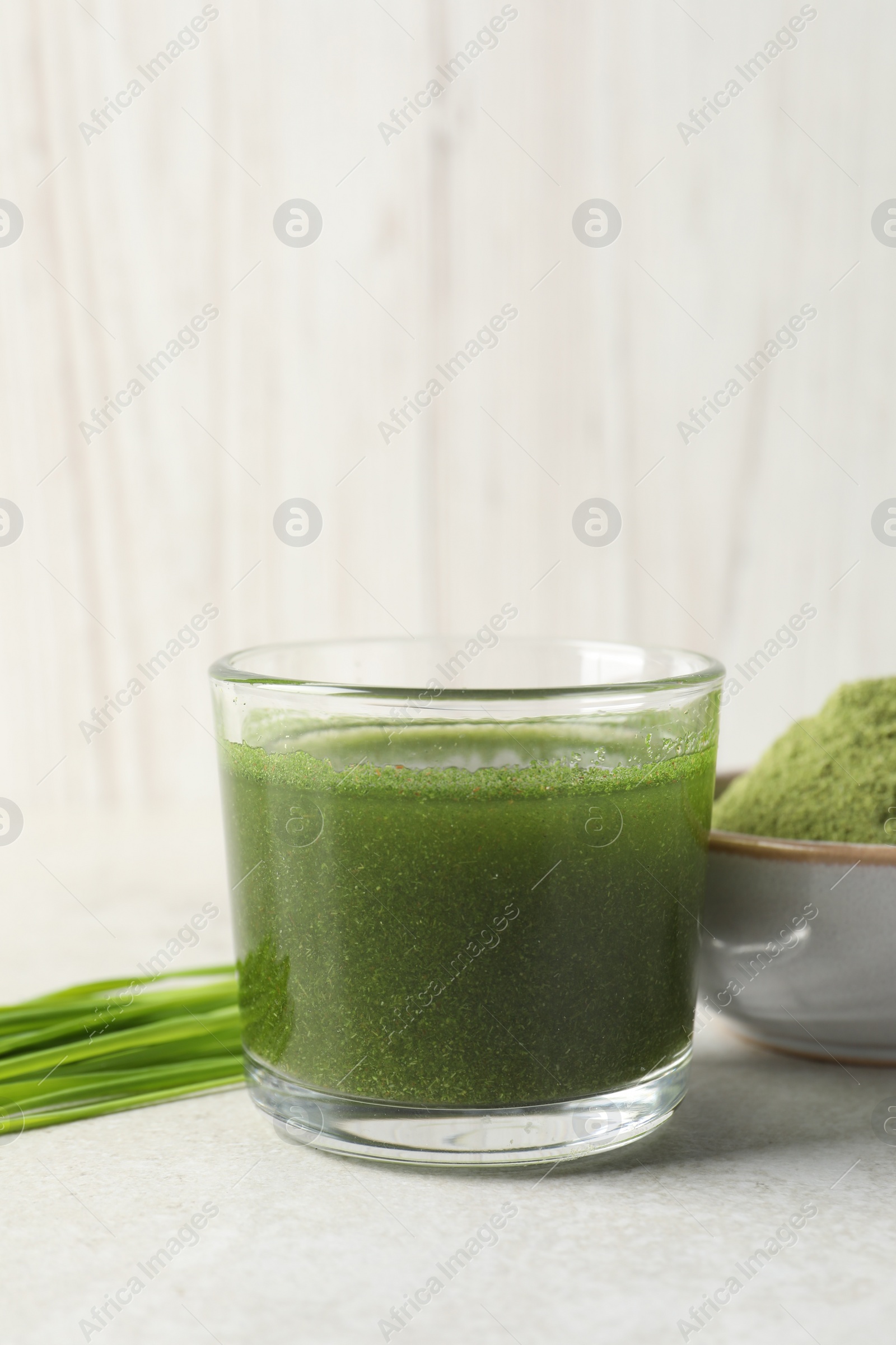 Photo of Wheat grass drink in glass, fresh sprouts and bowl of green powder on light table