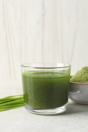 Photo of Wheat grass drink in glass, fresh sprouts and bowl of green powder on light table