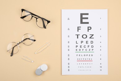 Photo of Vision test chart, glasses, lenses and tweezers on beige background, flat lay