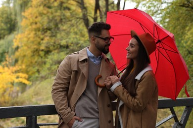 Happy young couple with red umbrella spending time together in autumn park, space for text