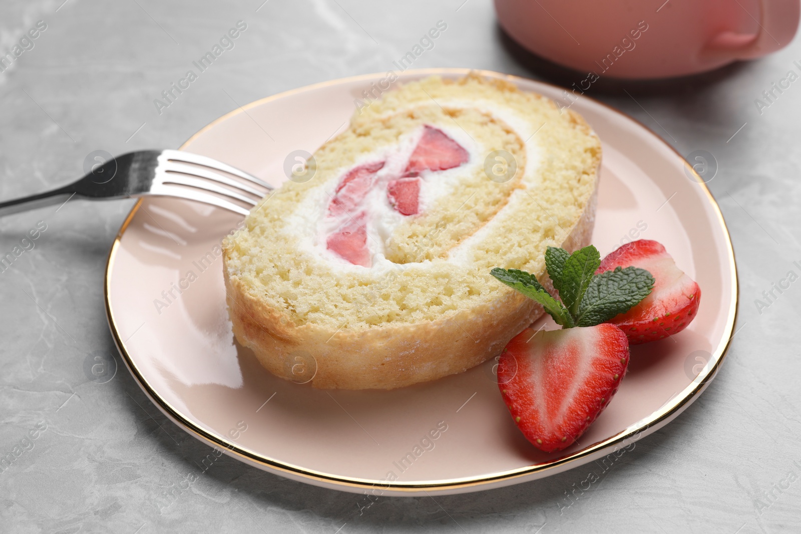 Photo of Slice of delicious sponge cake roll with strawberries and cream served on light grey table, closeup