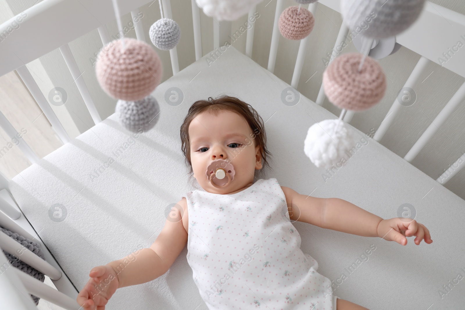 Photo of Cute little baby lying in crib with hanging mobile